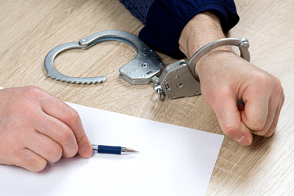 A man writes a confession at the police station. One hand is cuffed, the other is unbuttoned, pen in hand for writing explanations. Arrest, bail, felon, jail. the criminal's fingerprints