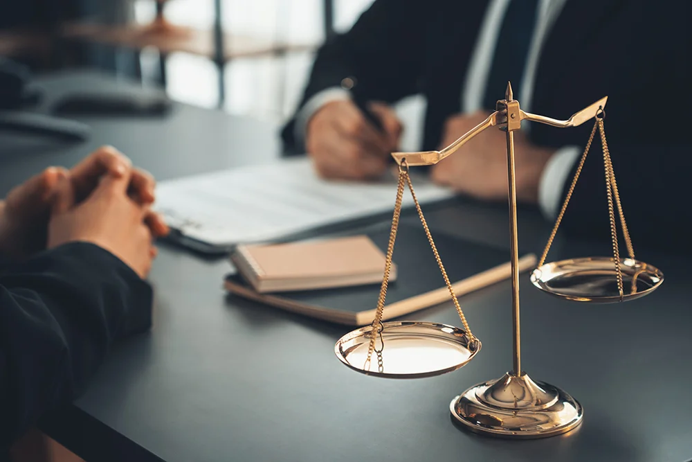 Focus shiny golden balanced scale on blurred background of lawyer colleagues working on desk at law firm office. Scale balance for righteous and equality judgment by lawmaker and attorney. Equilibrium