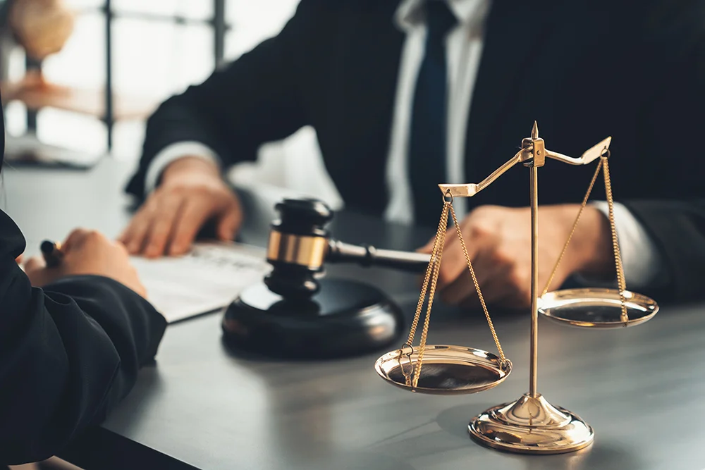 Focus shiny golden balanced scale on blurred background of lawyer colleagues working on desk at law firm office. Scale balance for righteous and equality judgment by lawmaker and attorney. Equilibrium