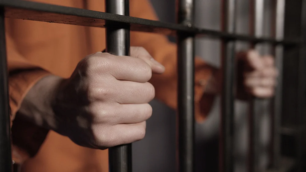 Caucasian man's hands on the bars of a prison cell