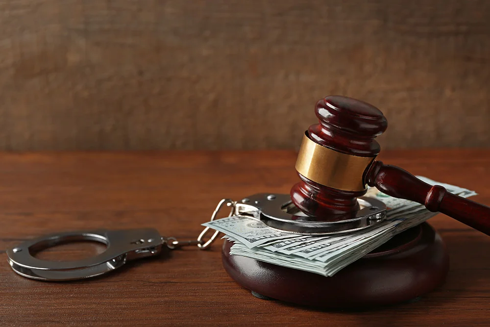 Law gavel with dollars and handcuffs on wooden table background, closeup